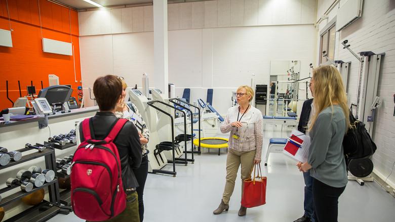 vrouw geeft uitleg in zaal met fitnesapparatuur